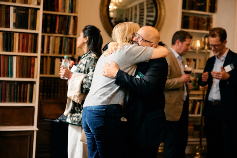Two guests greeting one another among the bookshelves at The Emergence