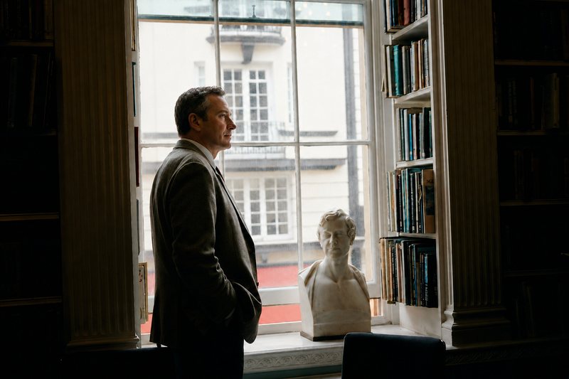 A leader standing alone at a tall window in the library at The Emergence, looking out over the street below